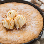 A thick and chewy snickerdoodle cake baked in a cast iron skillet and topped with ice cream and caramel sauce.